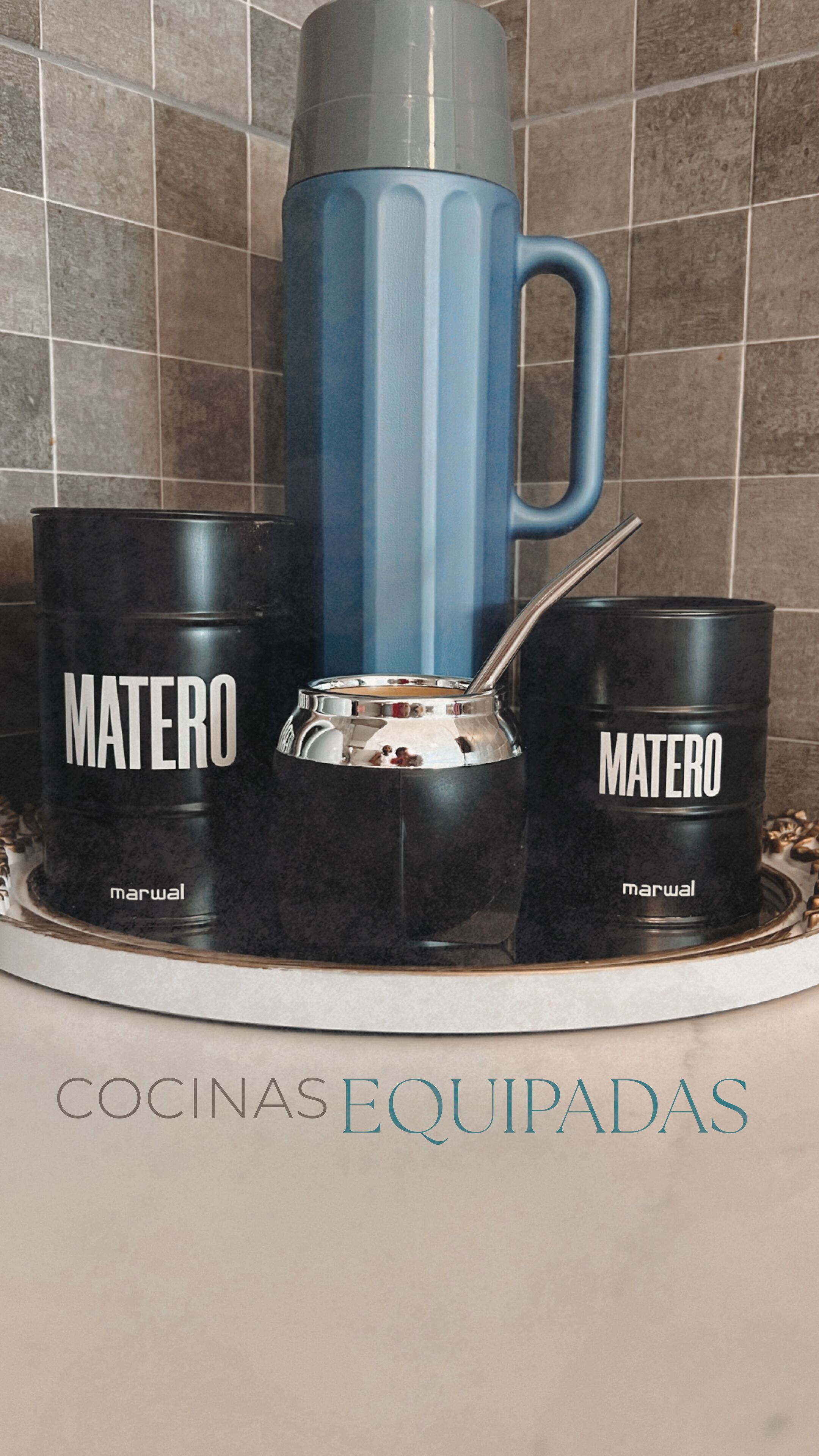 A kitchen setup with a blue mug, two black mugs labeled 'MATERO', and a silver coffee pot on a tray.