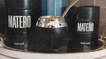 A kitchen setup with a blue mug, two black mugs labeled 'MATERO', and a silver coffee pot on a tray.