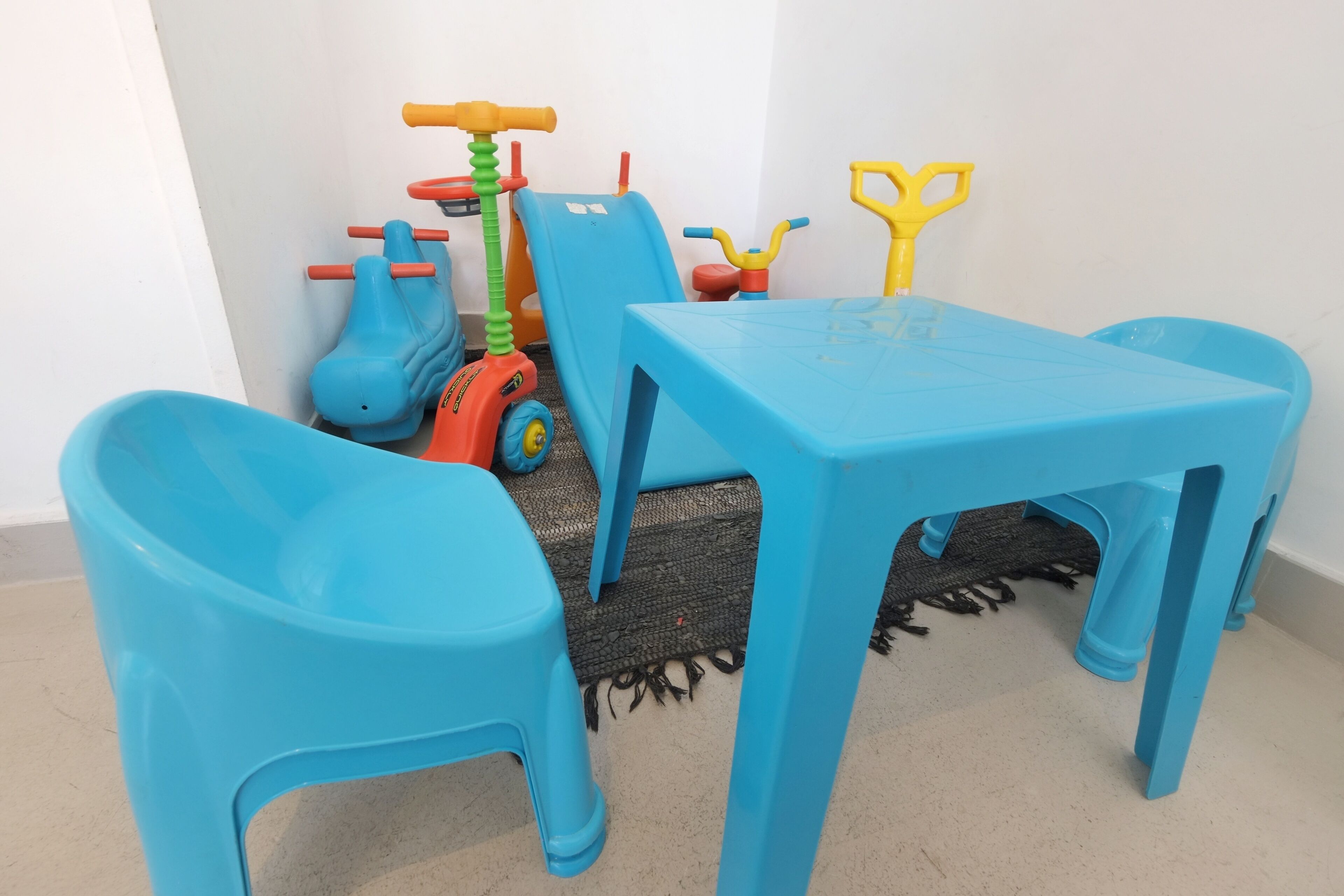 A room with a blue table and matching chairs, a small toy car, and a yellow toy.