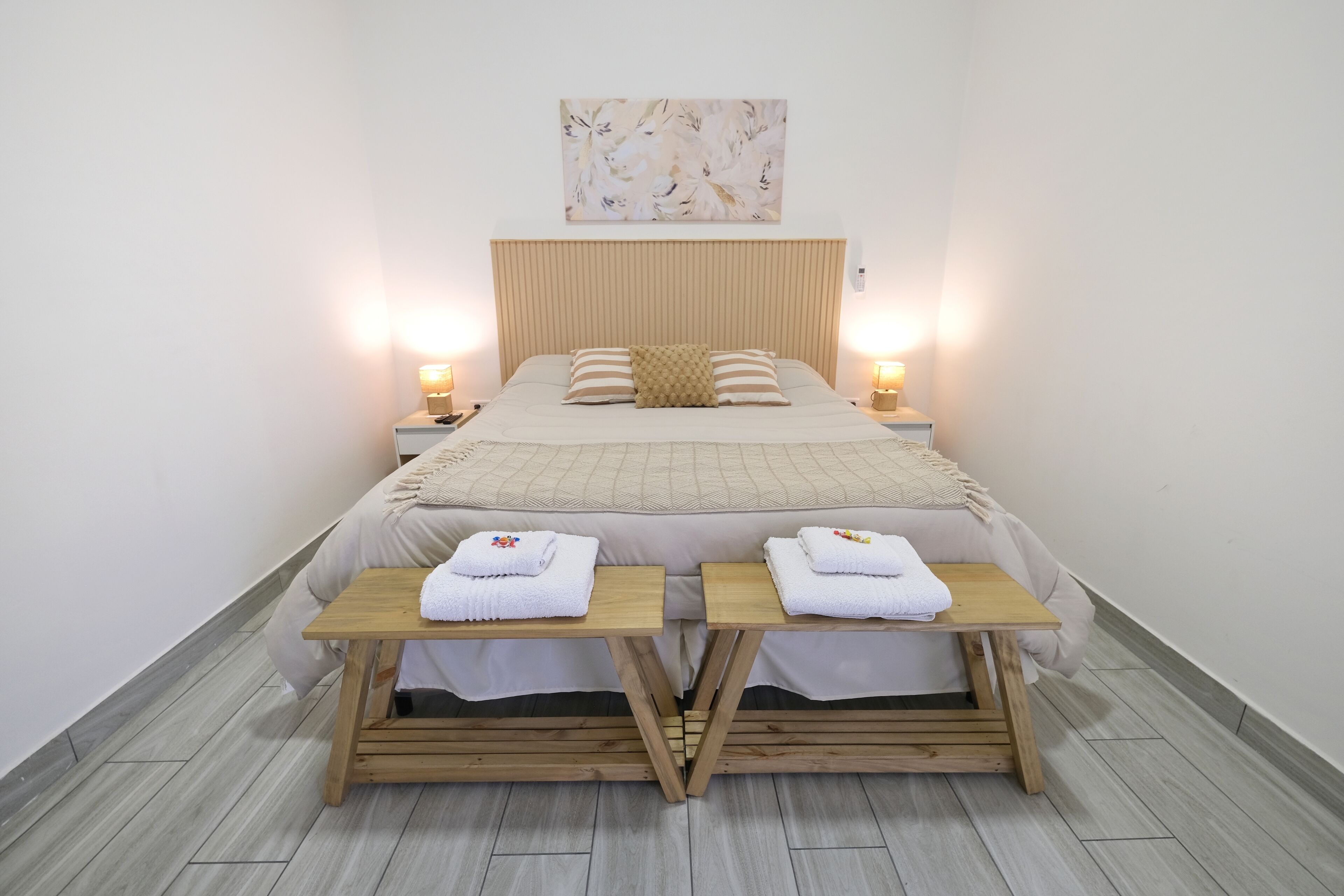 Une chambre d’hôtel bien aménagée, avec un grand lit, deux tables de chevet avec des serviettes, une tête de lit et une œuvre d’art accrochée au mur.