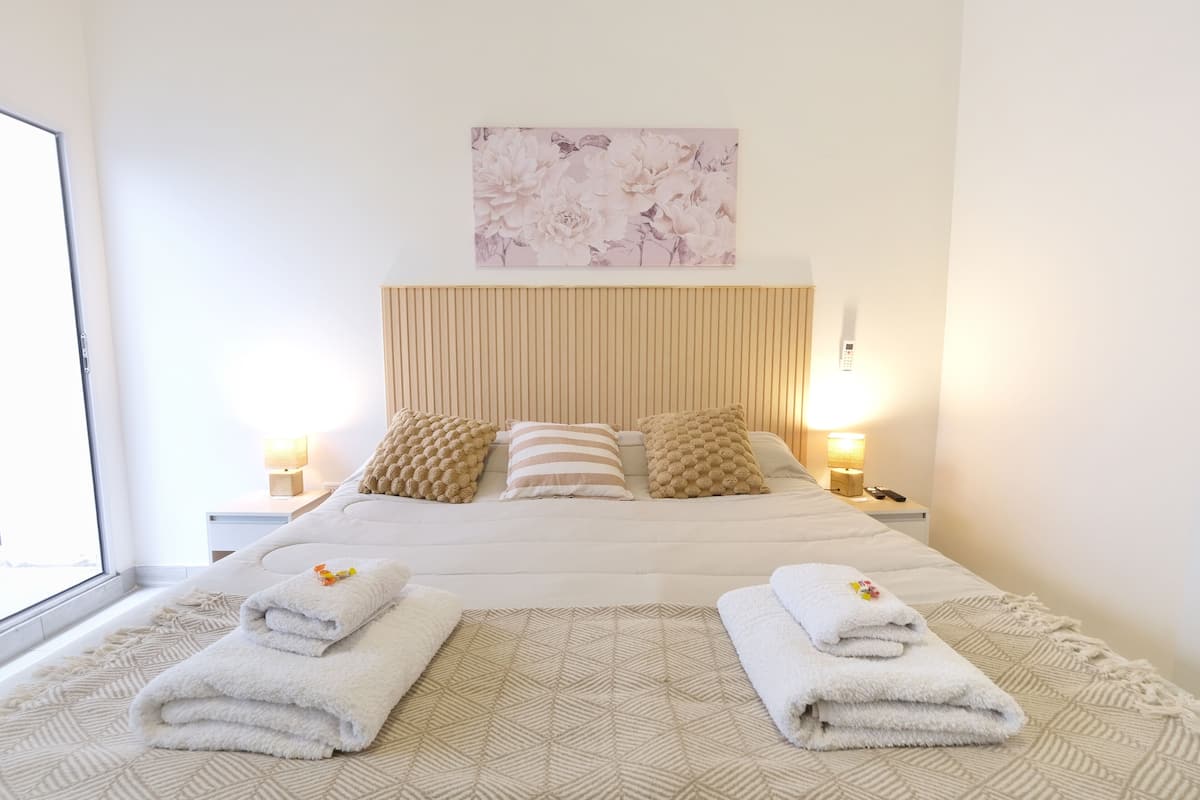 A neatly made bed with a geometric patterned bedspread, two pillows, and two folded towels on the side.