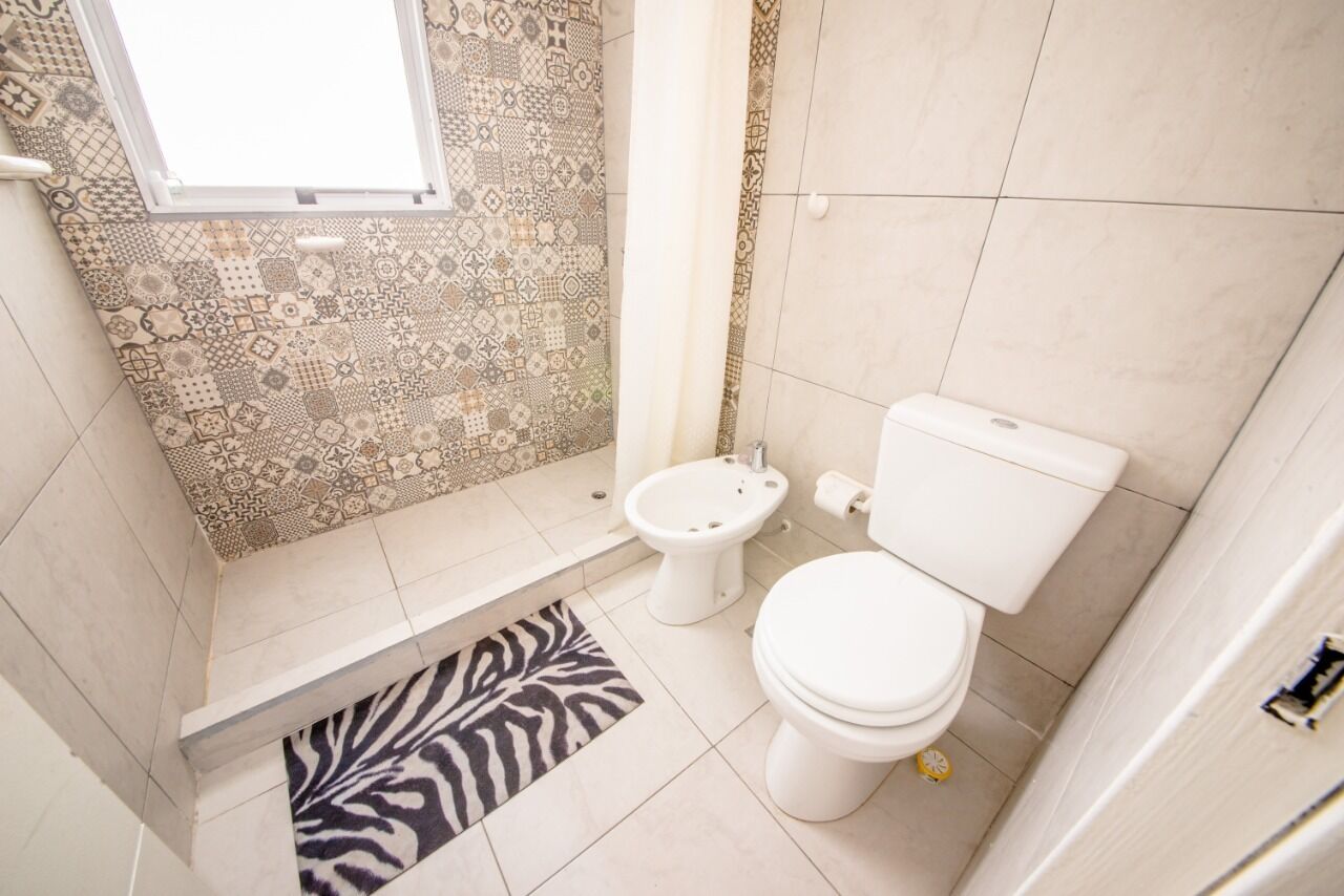 Une salle de bain avec des carreaux à motifs, un tapis à rayures zébrées, des toilettes et un bidet.