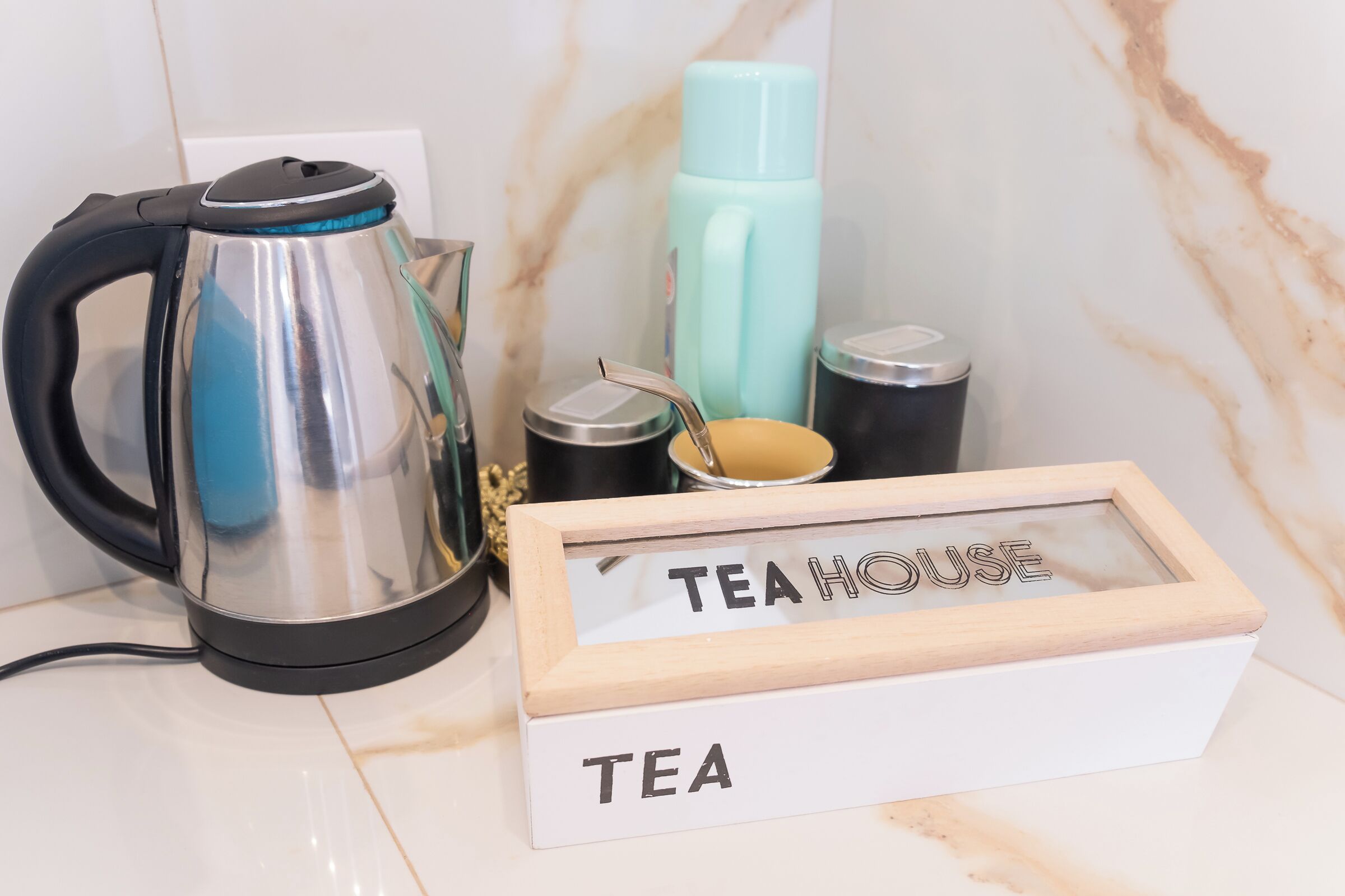 Eine Küchenzeile mit Wasserkocher, Thermoskanne und einer Teebox mit dem Aufdruck 'TEAHOUSE'.