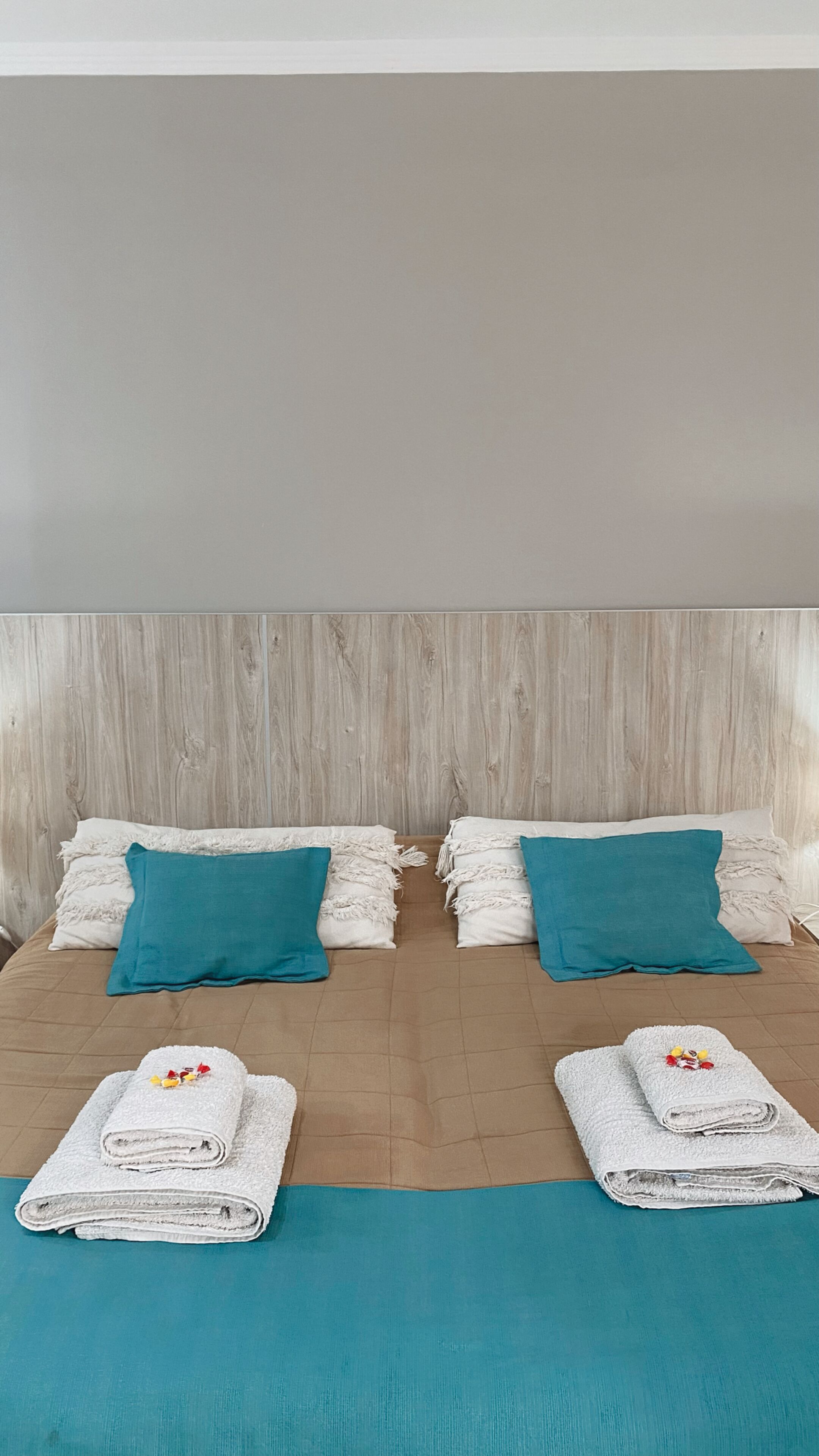 A double bed with two pillows, a wooden headboard, and two folded towels on the bed.