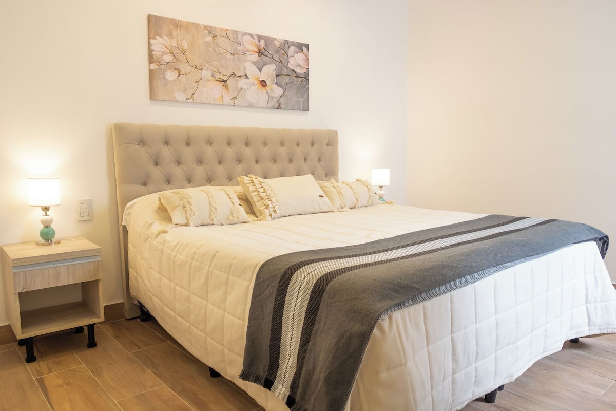 A neatly made bed with a tufted headboard, two bedside tables with lamps, and a floral painting on the wall.