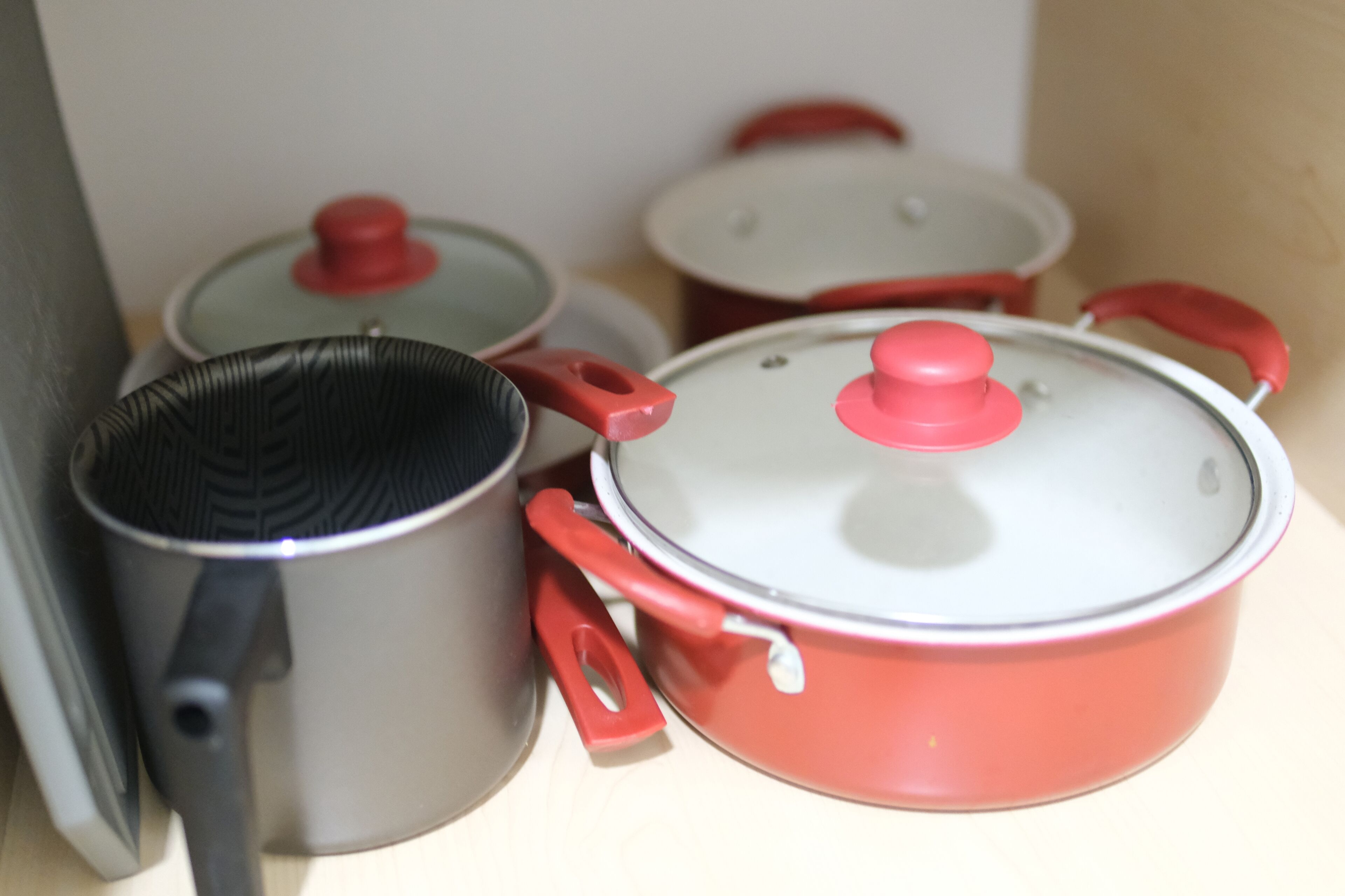 Four kitchen pots with lids, two with red handles and two with black handles, placed on a countertop.