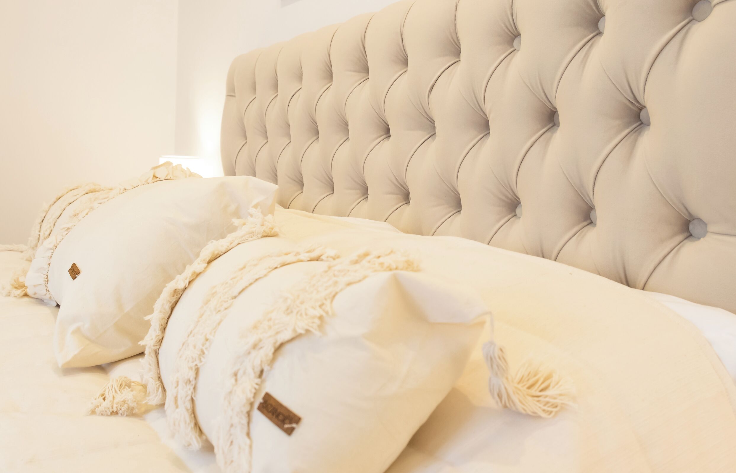 A bed with a tufted headboard, multiple pillows, and a textured blanket.