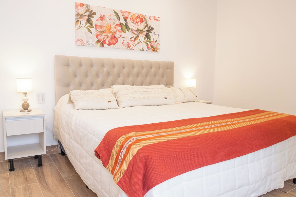 A neatly made bed with a red and white striped blanket, a tufted headboard, and a floral artwork above it.