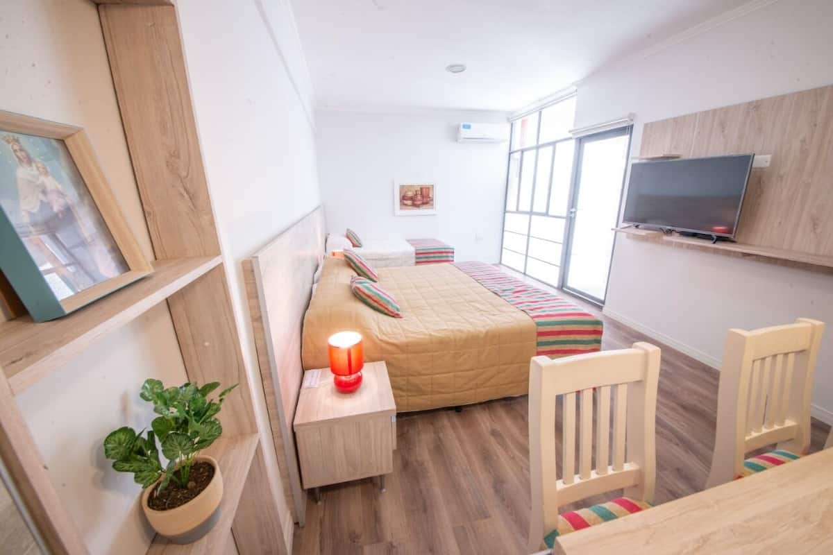 A compact bedroom with a bed, bedside table, lamp, and a TV mounted on the wall.