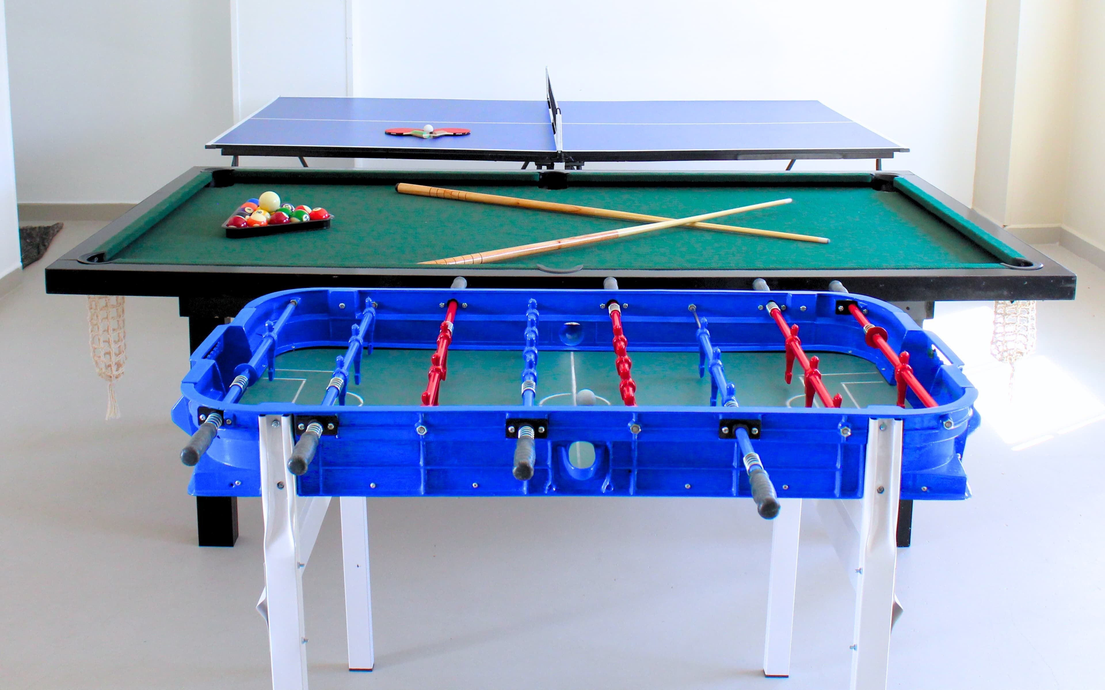 A foosball table with a pool table in the background.