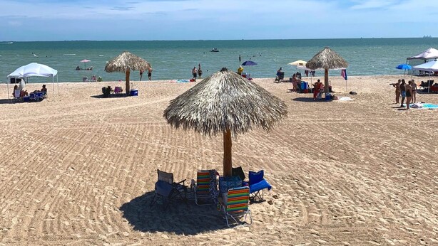 En strand med parasoller av halmtak, solstolar och folk som solar.