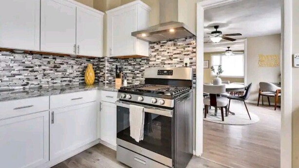 A modern kitchen with white cabinets, a stainless steel stove, and a patterned backsplash. - Sunny's Haven in Little Italy (Omaha)
