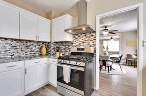 A modern kitchen with white cabinets, a stainless steel stove, and a patterned backsplash. - Sunny's Haven in Little Italy (Omaha)
