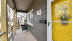 A covered porch with a yellow door, a mailbox, and a number sign. - Sunny's Haven in Little Italy (Omaha)