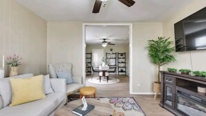 A living room with a sofa, coffee table, and a fireplace. There is a dining area in the background with a table and chairs. - Sunny's Haven in Little Italy (Omaha)