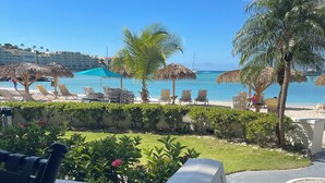A resort pool area with lounge chairs and umbrellas, a palm tree, and a view of the ocean. - Amazing Beachfront Condo in Simpson Bay -Walk Out Beach/Pool (Philipsburg)