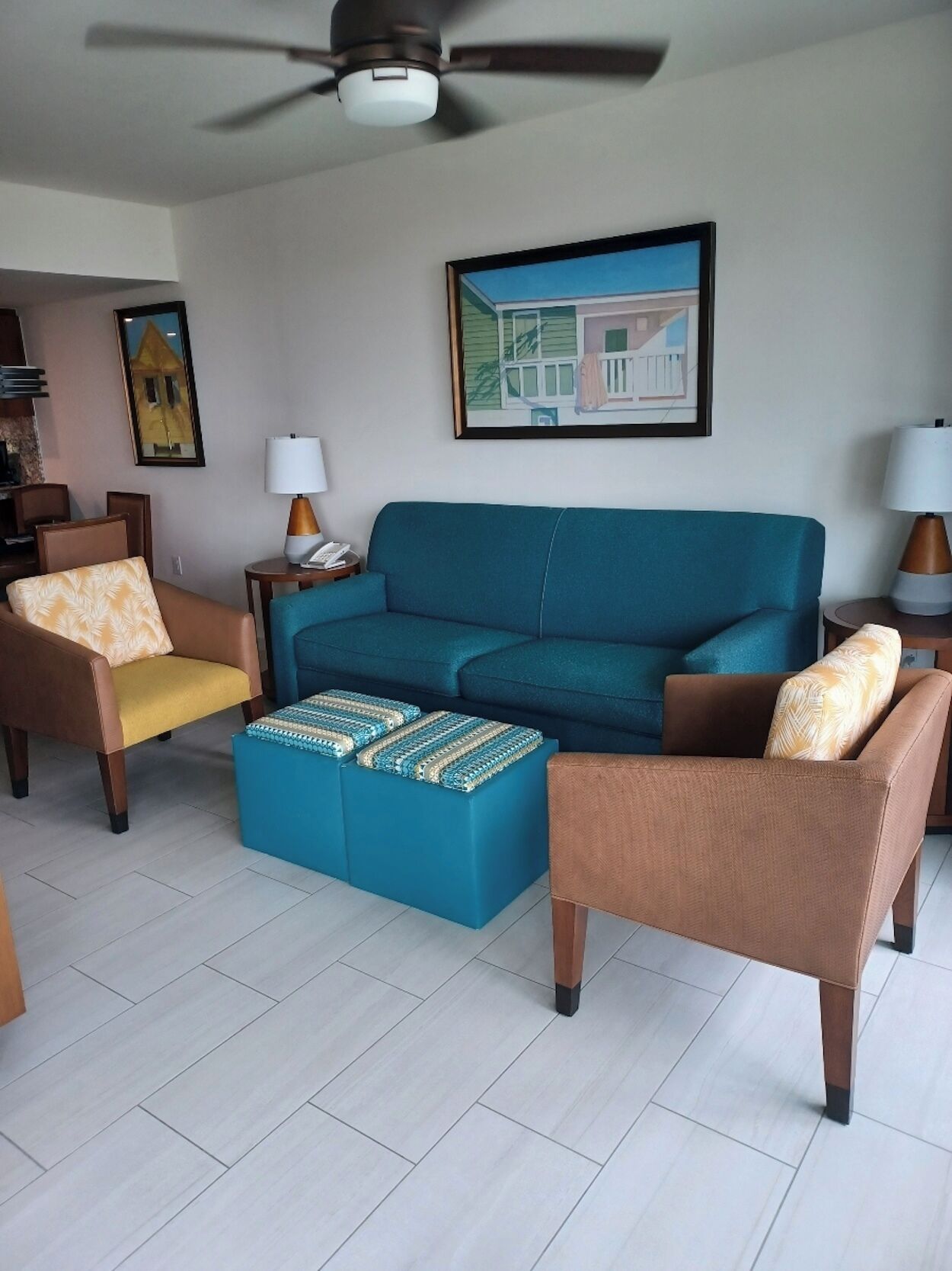 Ein Wohnzimmer mit blauem Sofa, zwei Sesseln, einem Couchtisch und einem Deckenventilator.