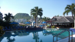 A pool area with lounge chairs, umbrellas, and a view of a mountain in the background. - Amazing Beachfront Condo in Simpson Bay -Walk Out Beach/Pool (Philipsburg)