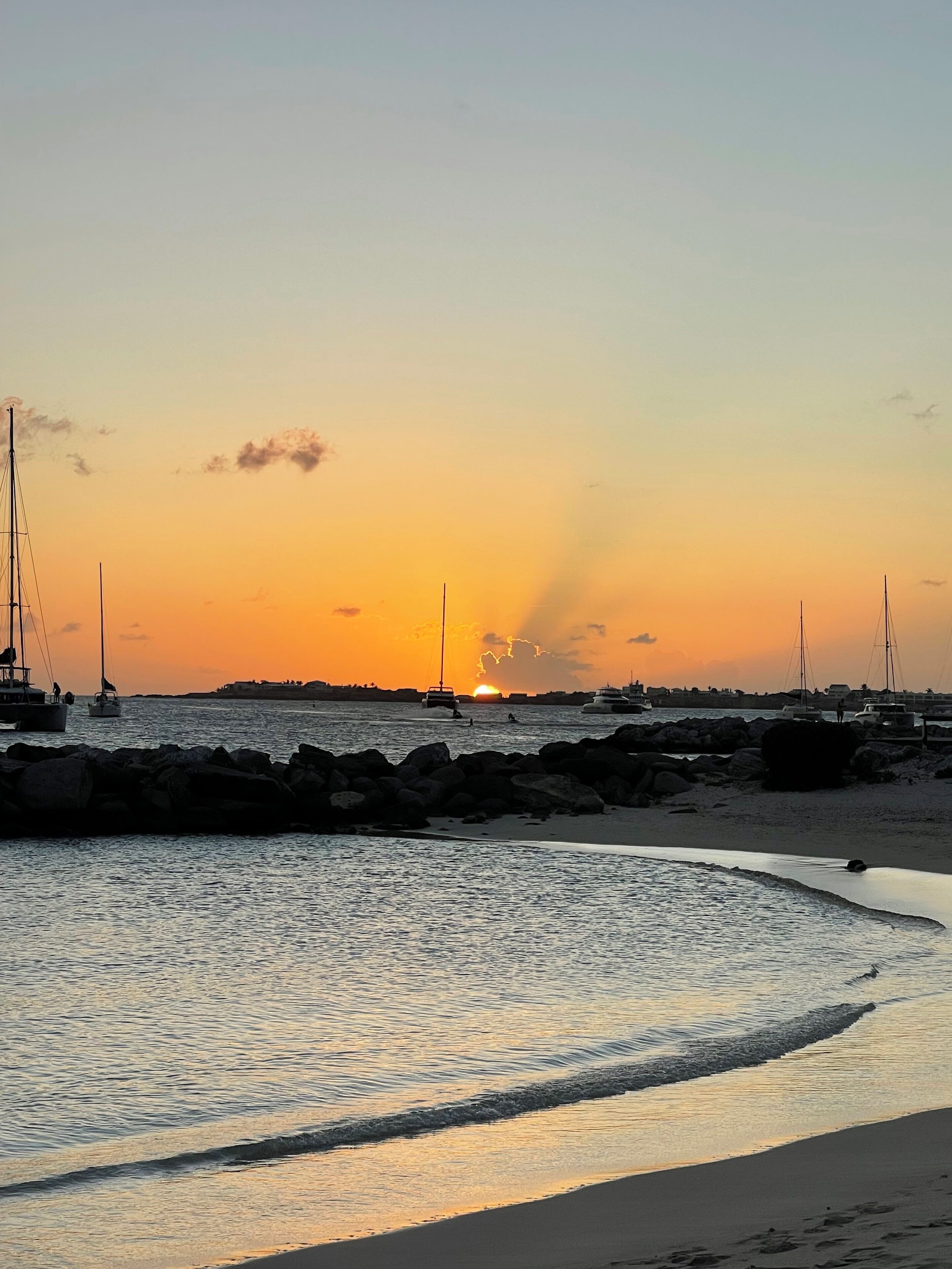 Een zandstrand met boten en een ondergaande zon.
