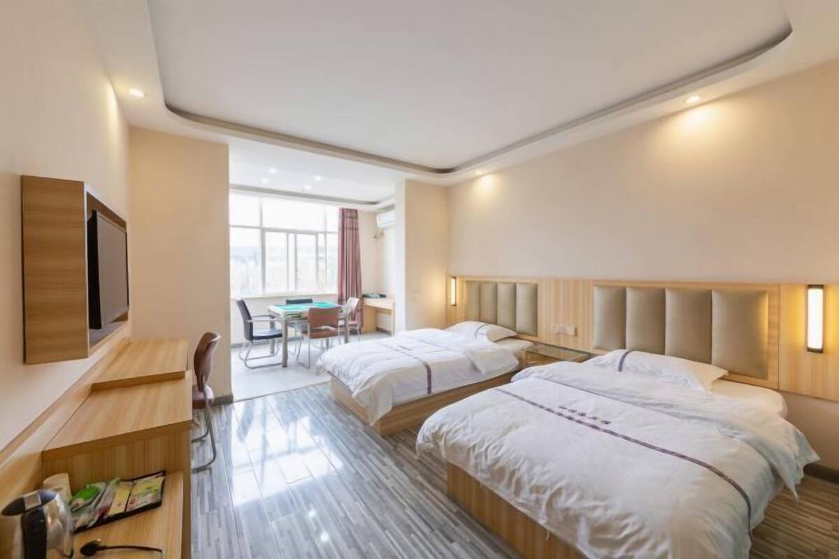 A hotel room with two beds, a desk, a chair, and a TV.