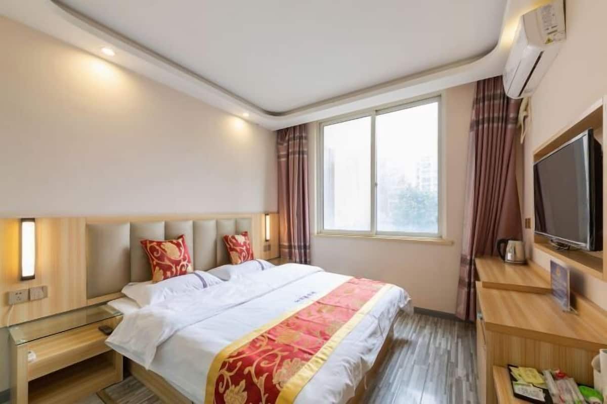 A hotel room with a bed, bedside table, TV, and a window with curtains.