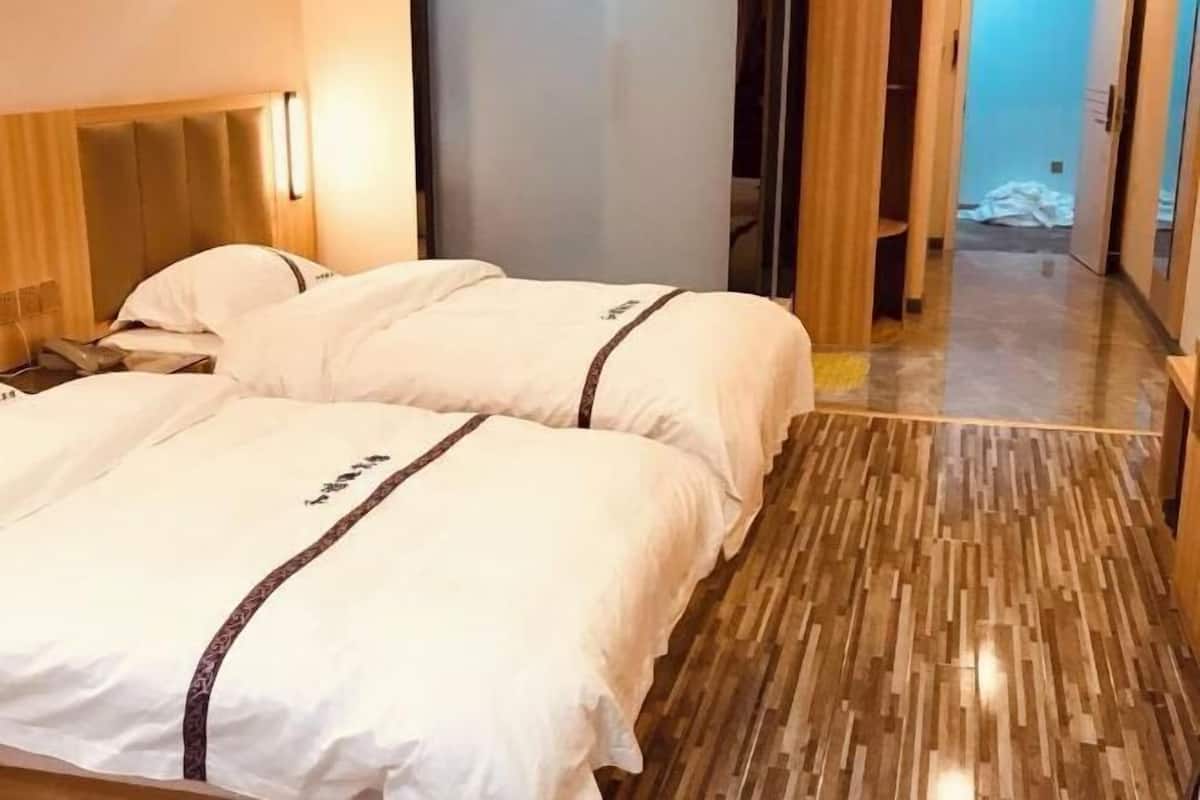 A hotel room with two beds, a wooden floor, and a visible door leading to another room.