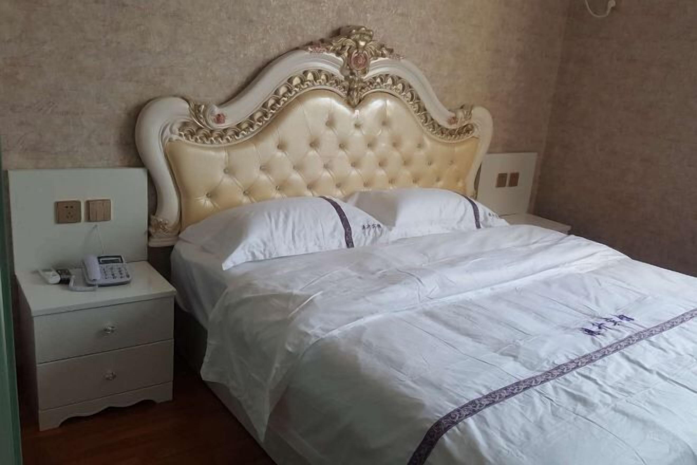 A bedroom with a tufted headboard, a white bedspread, a bedside table with a phone, and a nightstand.