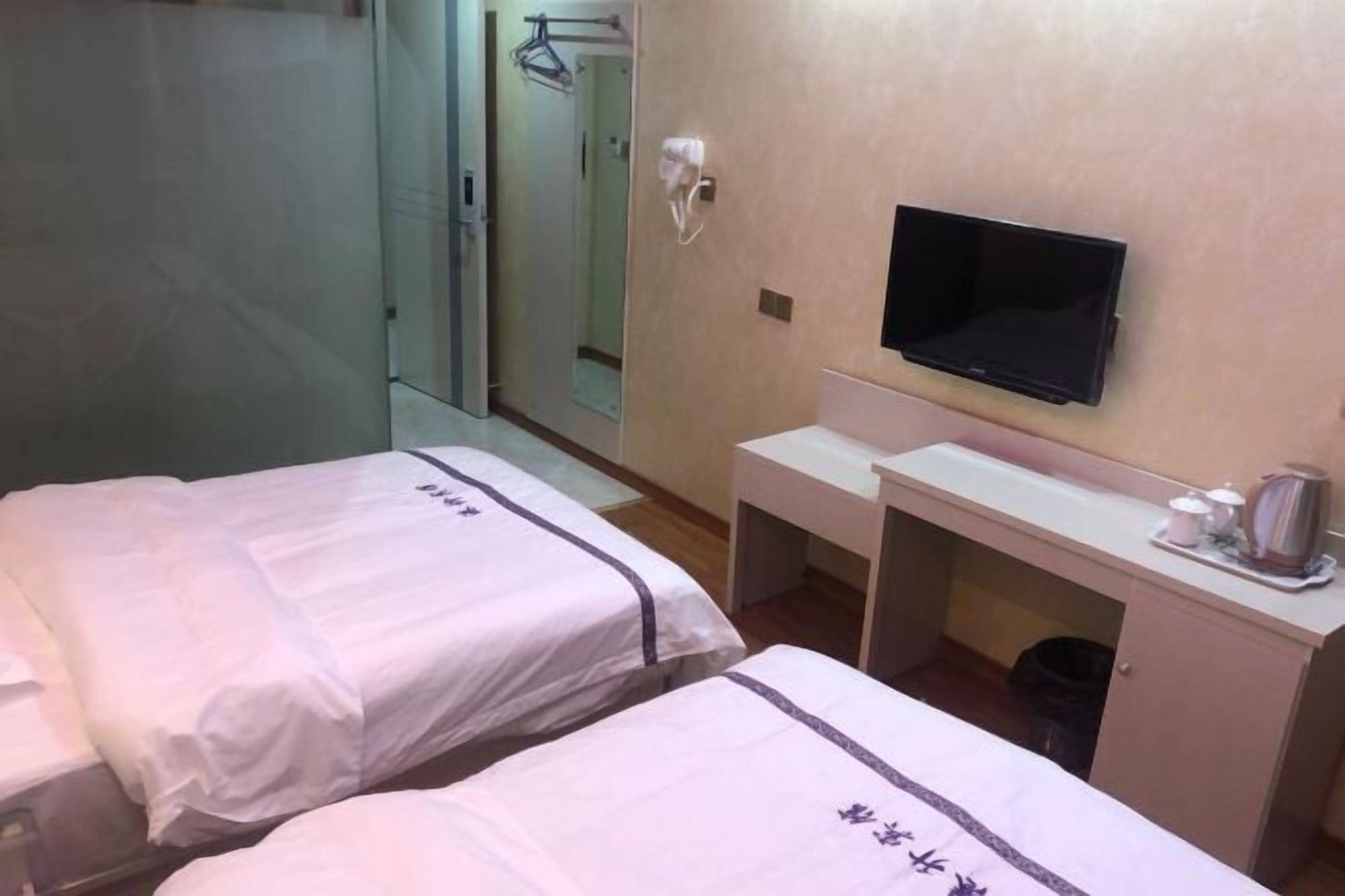 Ein Hotelzimmer mit zwei Betten, einem Schreibtisch, einem Fernseher und einem Spiegel.