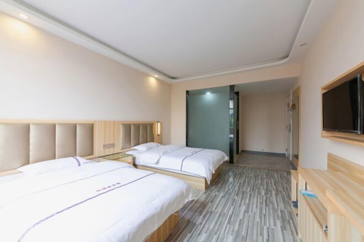 A hotel room with two beds, a wooden headboard, a flat-screen TV, and a wooden bench.