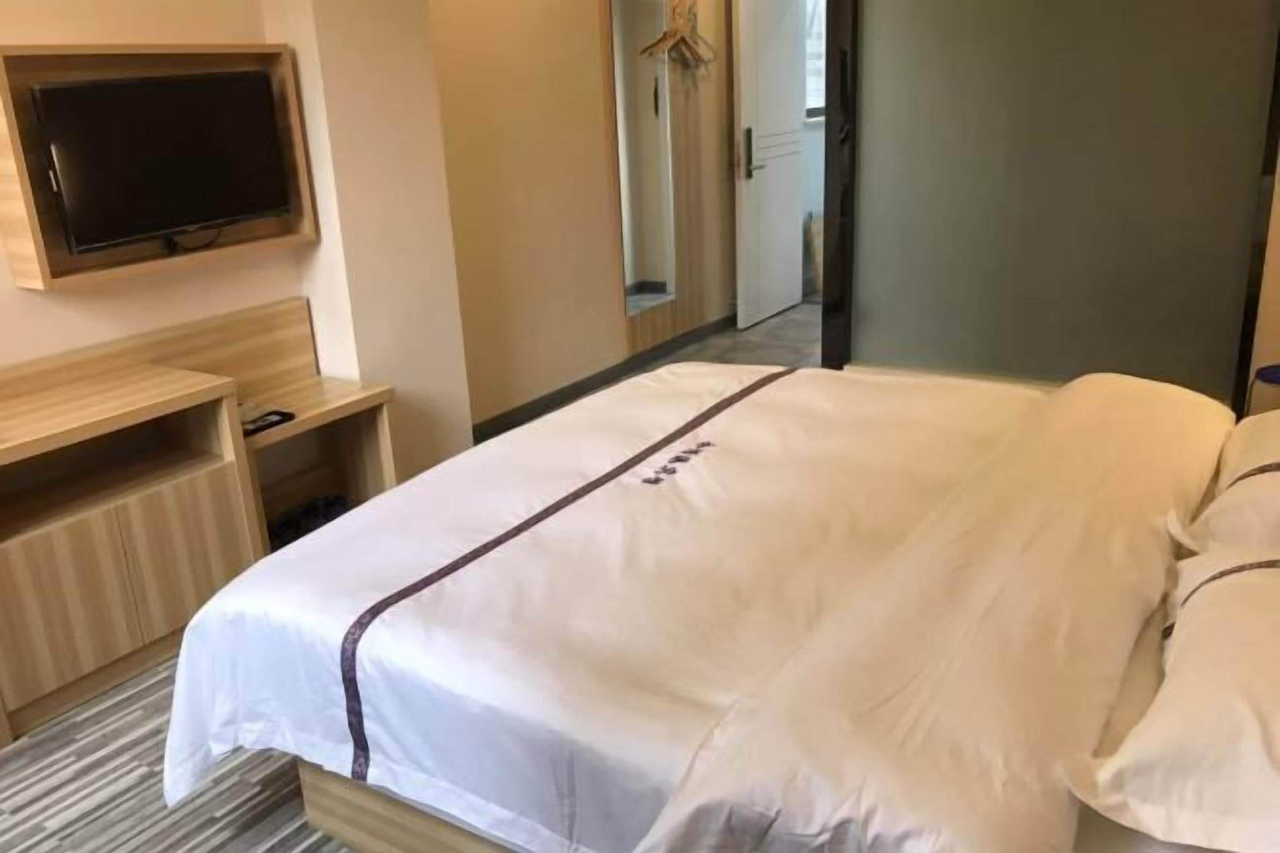 A hotel room with a bed, a TV mounted on the wall, and a mirror.