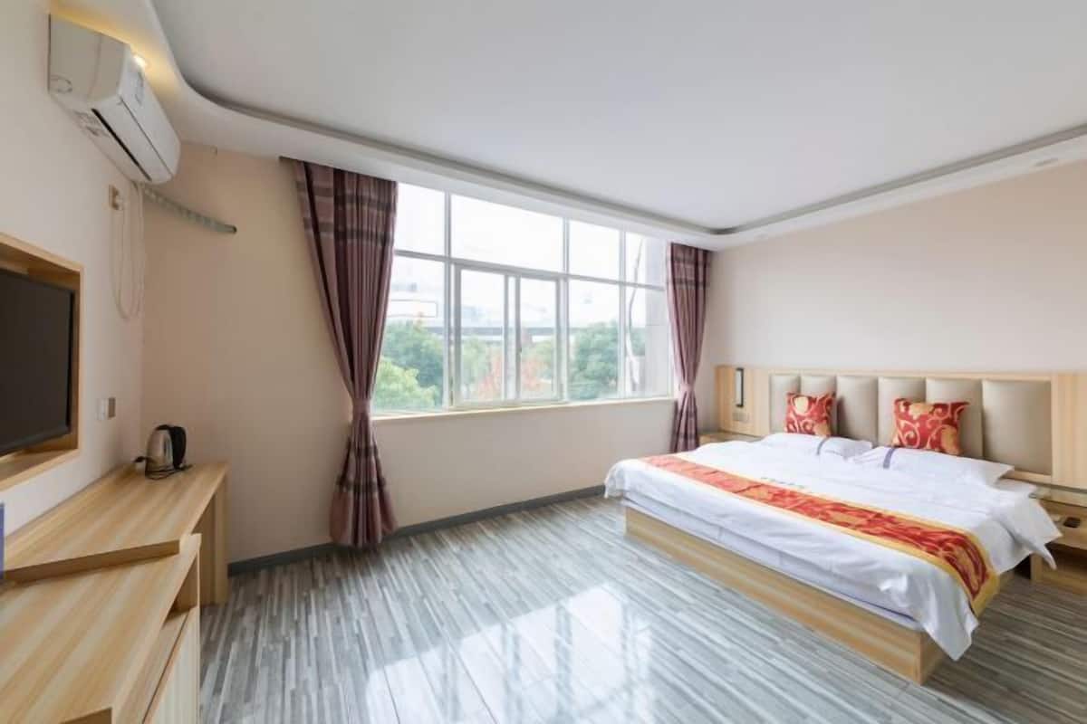 A hotel room with a bed, a TV, a desk, and a window with curtains.