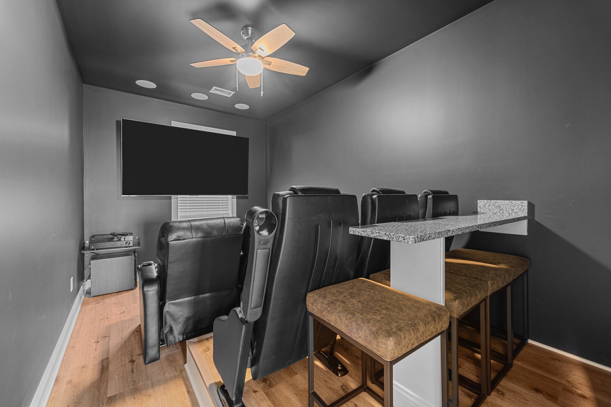 Habitación compacta con ventilador de techo, televisor de pantalla plana, una pequeña cocina americana y una zona de estar con dos sillas y un banco.