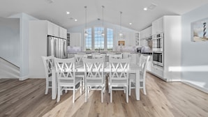 A modern kitchen with white cabinetry, a central island with chairs, and large windows. - Soundfront 10BR with Pool & Hot Tub- Perfect for Large Groups ★★★★★ (Avon)