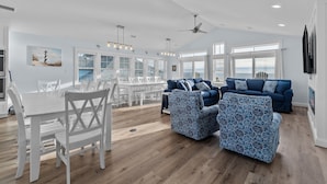 A spacious living area with a dining table and chairs, a blue sofa, and a ceiling fan. - Soundfront 10BR with Pool & Hot Tub- Perfect for Large Groups ★★★★★ (Avon)