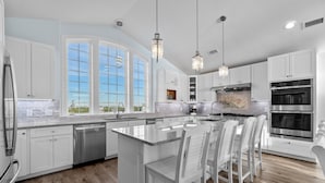 A modern kitchen with white cabinetry, a large island with bar stools, stainless steel appliances, and pendant lighting. - Soundfront 10BR with Pool & Hot Tub- Perfect for Large Groups ★★★★★ (Avon)
