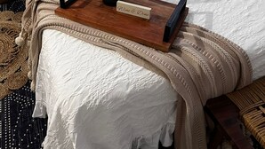 Una cama cuidadosamente tendida, una botella de champán, una bandeja con un cartel y una almohada con la inscripción 'Barefoot Welcome'.