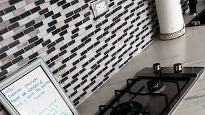 Una cocina con estufa a gas, salpicadero con azulejos blanco y negro, y un letrero con un mensaje en español.