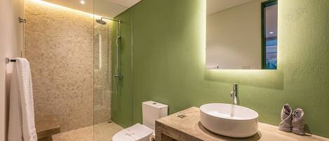 Une salle de bain avec une douche à parois de verre, des toilettes blanches, un lavabo avec un miroir et un mur vert.