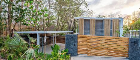 Un bâtiment moderne, doté d’une clôture en bois, d’une allée pavée et entouré de verdure.