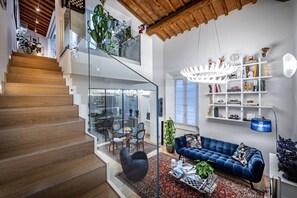 Een modern interieur met een trap, een woonkamer met een blauwe bank en een glazen balustrade.