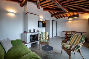 Ein gemütliches Wohnzimmer mit einem grünen Sofa, Korbstühlen, einem Kamin und einem an der Wand befestigten Flachbildfernseher.