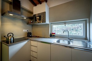 Eine moderne Küche mit einer Edelstahl-Dunstabzugshaube, einer integrierten Mikrowelle, einem Fenster mit Blick auf Bäume und einem Spülbecken mit Armatur.