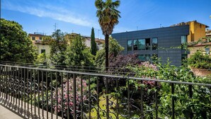 Ein Balkon mit schmiedeeisernem Geländer, üppiger Bepflanzung und einem modernen Gebäude im Hintergrund.