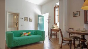 Una sala de estar con un sofá verde, una mesa de comedor de madera, sillas y una ventana con cortinas.
