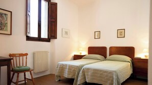 Un dormitorio con dos camas individuales, una silla de madera, un escritorio y un radiador.