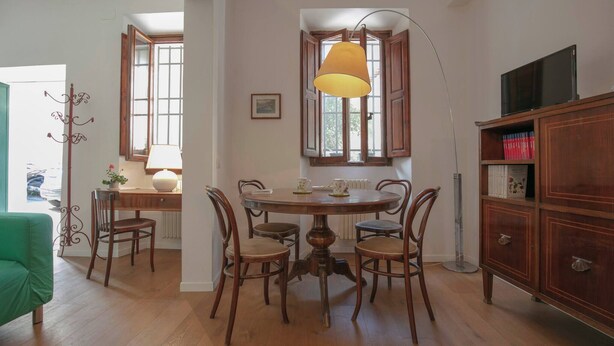Un comedor con una mesa redonda de madera, cuatro sillas, una lámpara y una estantería.