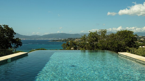 An infinity pool with clear blue water, surrounded by greenery and overlooking a coastal landscape with mountains in the distance. - Villa Napoleon, vue mer Exceptionnelle, Grande Piscine à Debordement (Pietrosella)