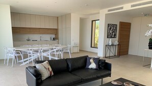 A modern living room with a black leather sofa, a coffee table, and a dining area with white chairs and a wooden table. - Villa Napoleon, vue mer Exceptionnelle, Grande Piscine à Debordement (Pietrosella)