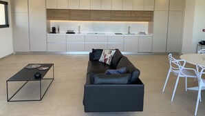 A modern kitchen with integrated appliances, a dining area with a white table and chairs, and a black leather sofa with cushions. - Villa Rivoli - Domaine Napoleon Corsica vue mer Exceptionnelle Grande Piscine (Pietrosella)