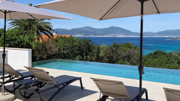 An infinity pool with lounge chairs and umbrellas, overlooking a coastal city and mountains. - Villa Rivoli - Domaine Napoleon Corsica vue mer Exceptionnelle Grande Piscine (Pietrosella)